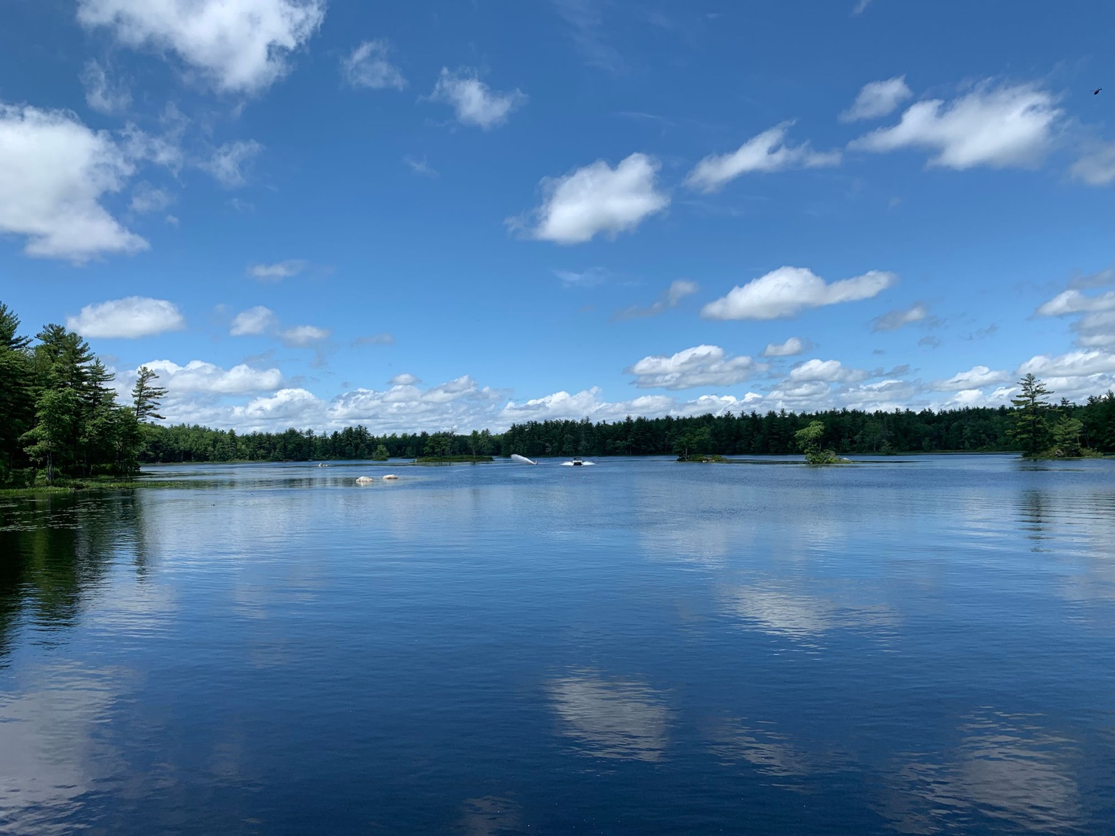 A boat pulling a skier across Dubes Pond on a summer day